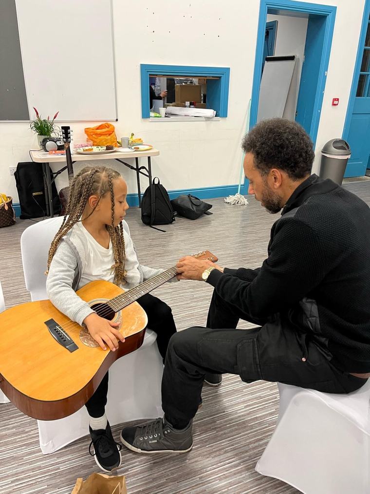 A volunteer teaches a child to play the guitar