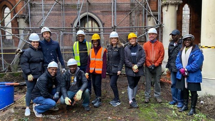 A large group of volunteers in hard hats in front of the scaffolded church