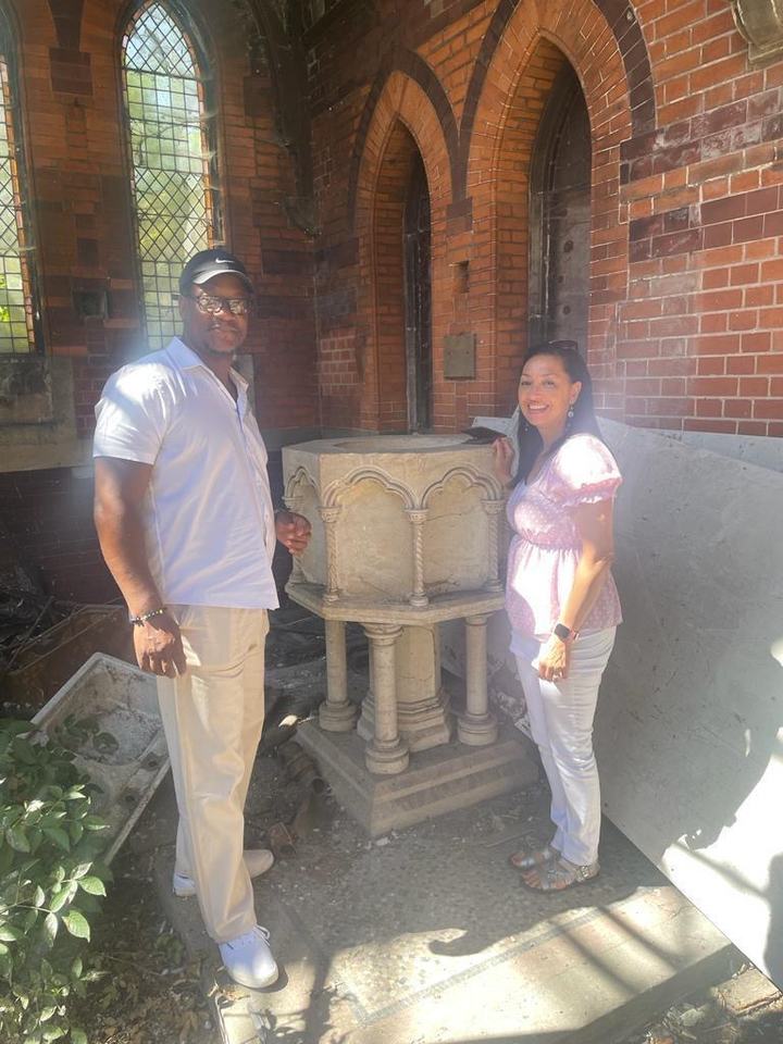 Two visitors beside the carved stone font