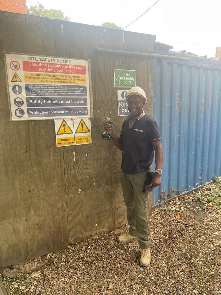 A volunteer in a hard hat with a drill beside the site safety notice